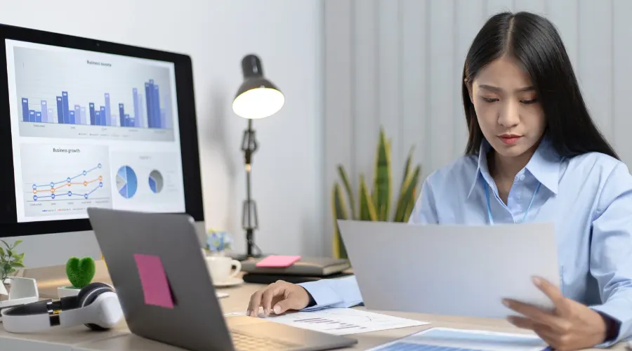 A girl taking an online test on laptop while holding notes and a pen for preparation